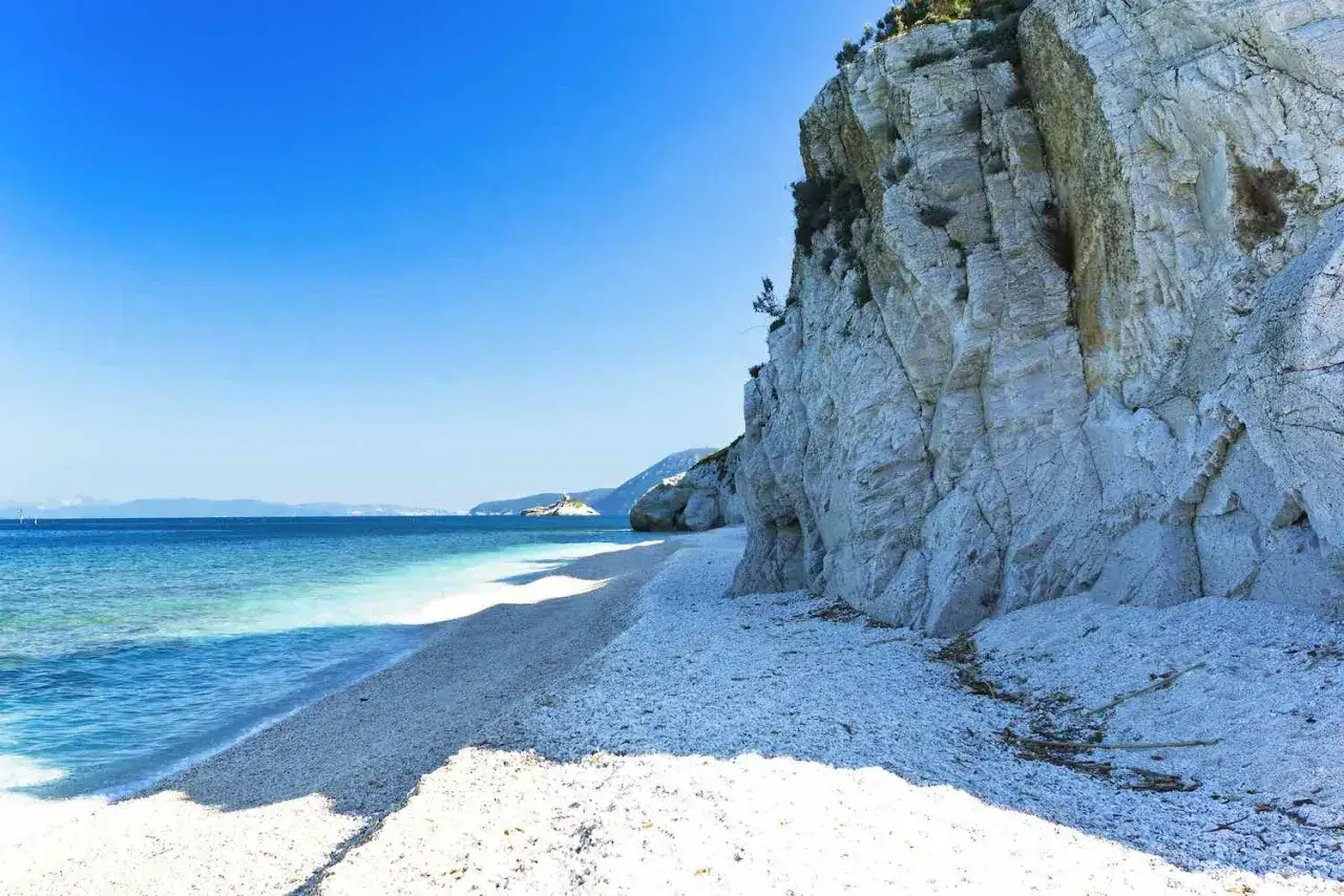 Spiaggia di ciottoli bianchi e mare cristallino sotto una scogliera imponente, un angolo di paradiso all'Isola d'Elba.