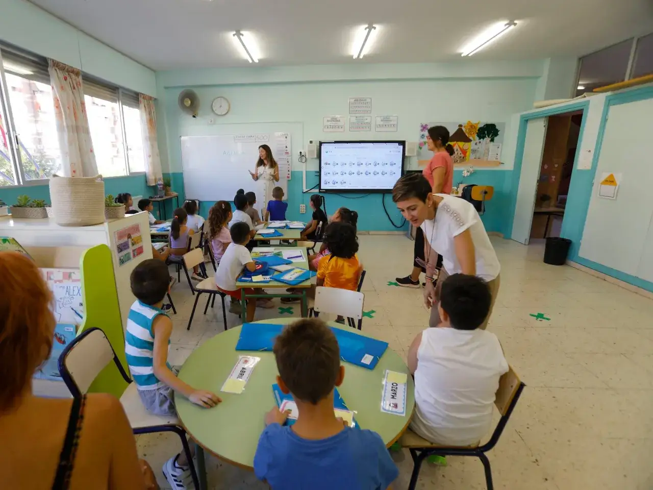 Ni&ntilde;os y maestros interact&uacute;an en un aula luminosa, promoviendo un ambiente de **colegio inclusivo** donde todos aprenden juntos.