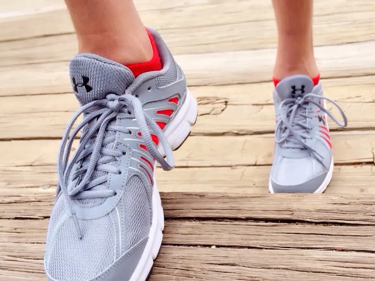 Bieganie z rwą kulszową jest możliwe, gdy masz odpowiednie buty. Szare buty sportowe z czerwonymi akcentami na drewnianej ścieżce.
