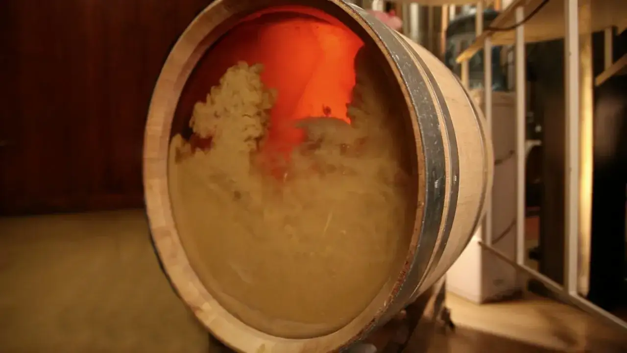 Holzfass mit tr&uuml;bem Wein, der sich auf der Hefe, sur lie, absetzt. Das Licht im Inneren des Fasses erzeugt eine warme, orangefarbene Glut.