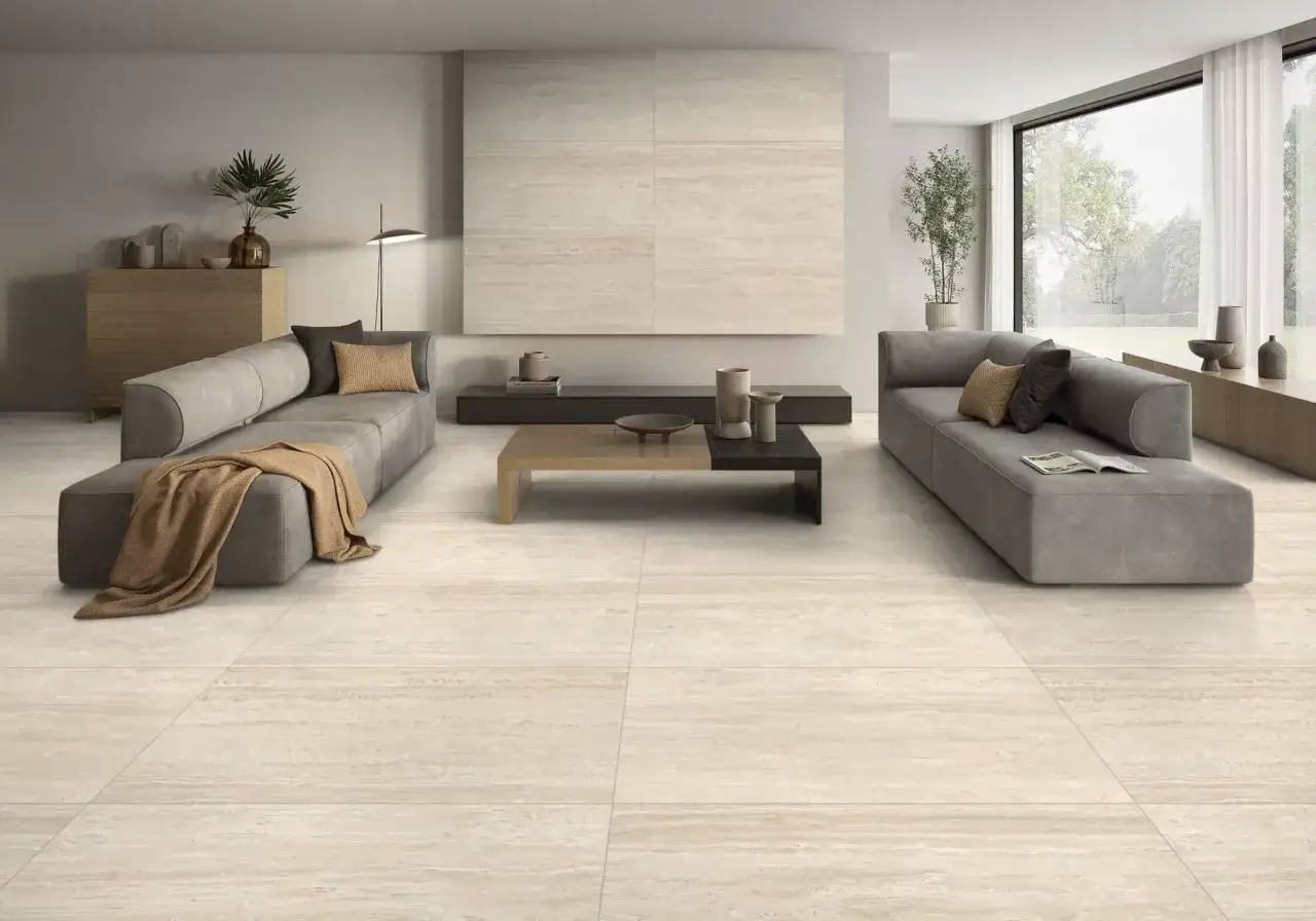 Un salon moderne aux canap&eacute;s gris, avec un sol et un mur en **travertin** aux tons chauds. Une table basse design et une grande fen&ecirc;tre ouvrant sur un jardin.
