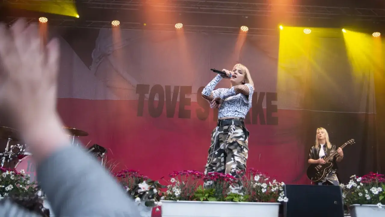 Tove Styrke sjunger på scenen med en gitarrist bredvid. En publikhand syns i förgrunden.