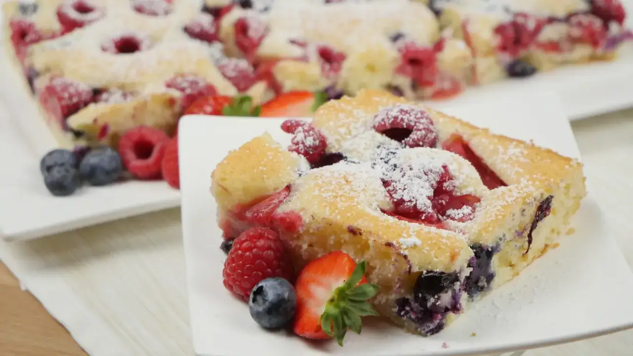 Ein saftiger Beerenkuchen mit Himbeeren, Blaubeeren und Erdbeeren, bestäubt mit Puderzucker. Perfekt für einen sommerlichen Genuss.