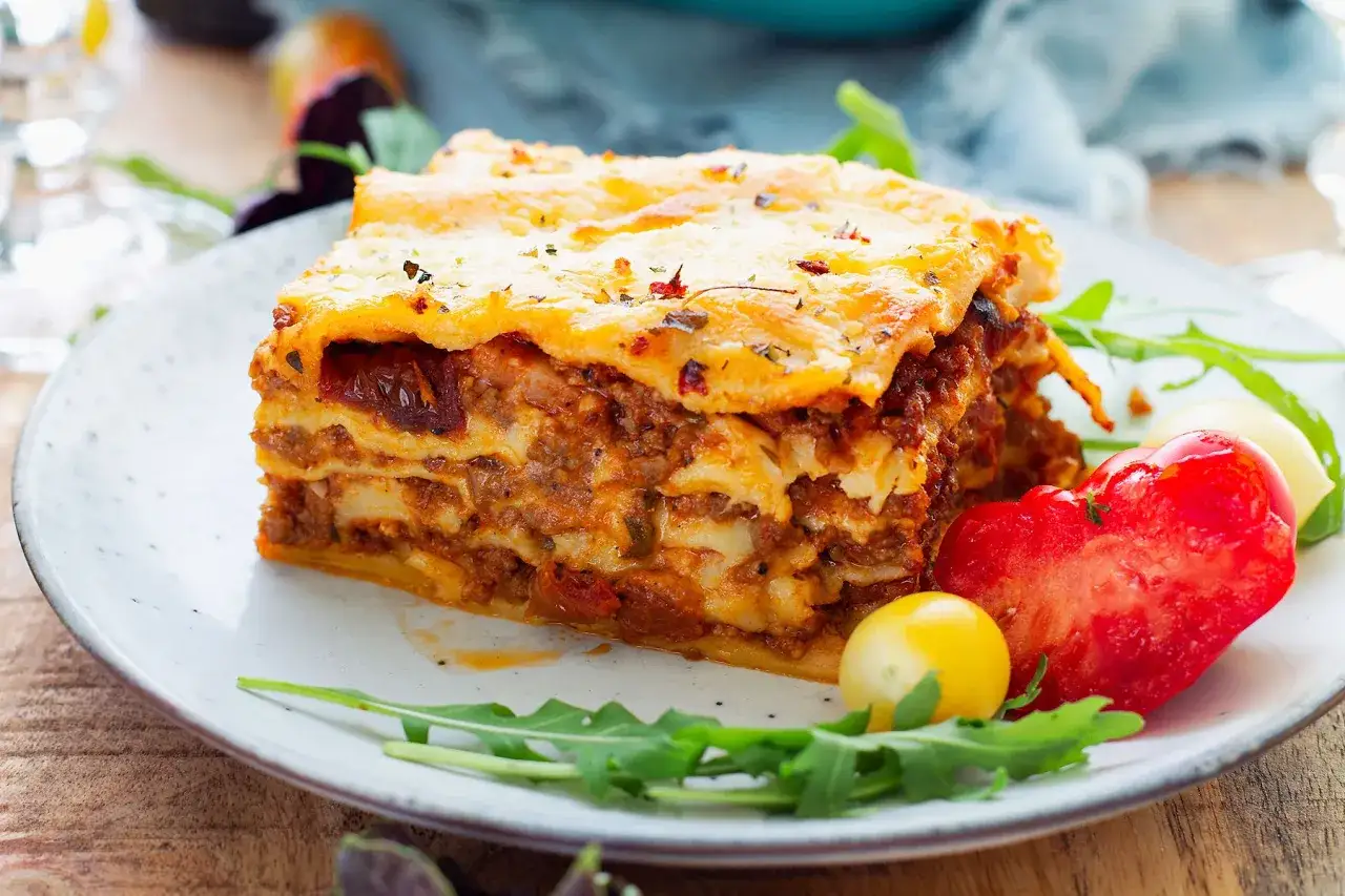 Pyszna, wielowarstwowa lasagne z mięsem mielonym i serem, podana z rukolą i pomidorkami. Idealna na obiad.