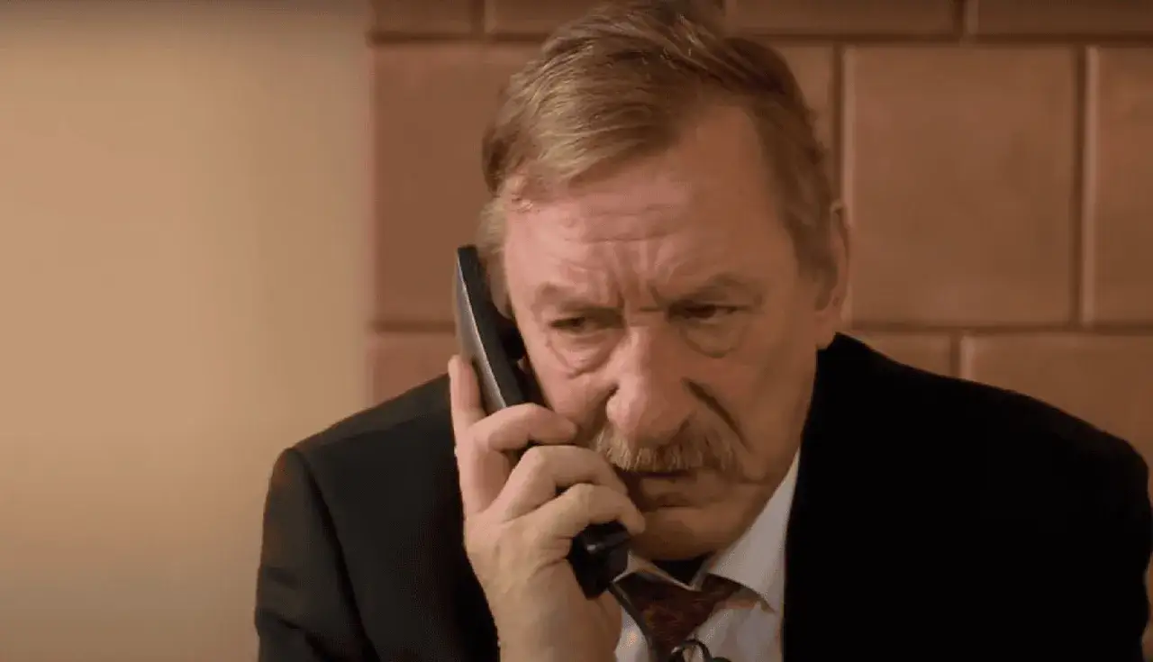 Sylwester Maciejewski w garniturze rozmawia przez telefon, marszcząc brwi.