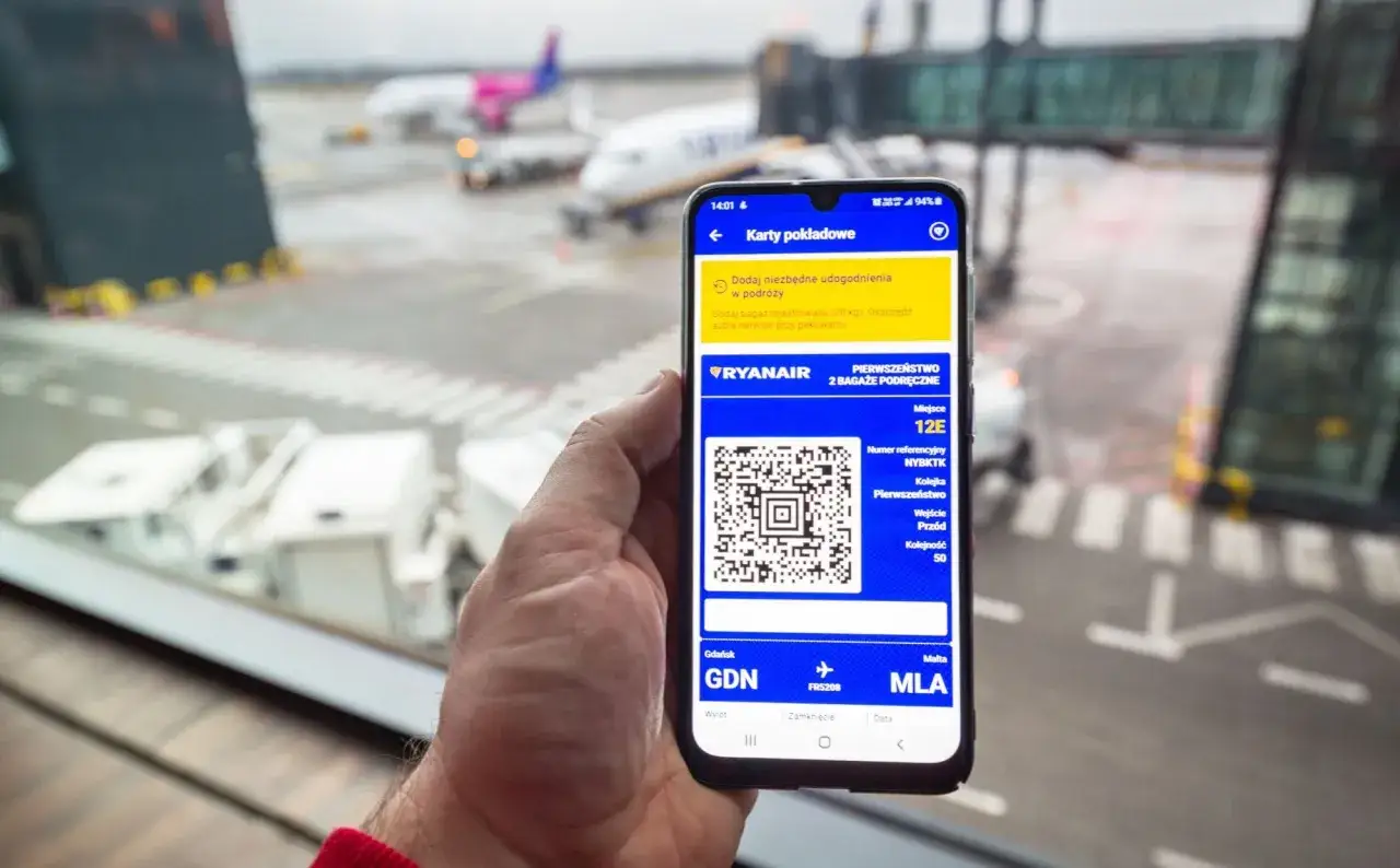 Odprawa na lotnisku Ryanair. Telefon pokazuje kartę pokładową z kodem QR i szczegółami lotu do Malty.