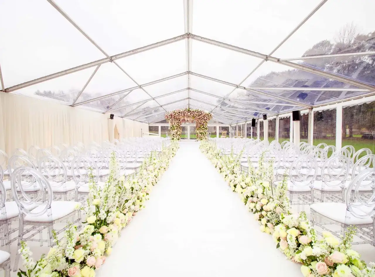 All&eacute;e de mariage sous tente transparente, d&eacute;cor&eacute;e de fleurs roses et blanches. Parfait pour un mariage pluie.
