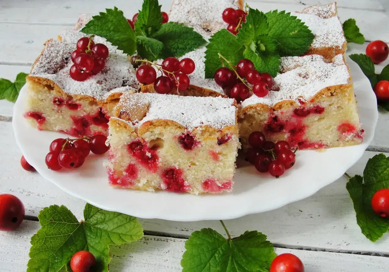 Szybkie ciasto z mrożonymi porzeczkami, posypane cukrem pudrem, ozdobione świeżymi porzeczkami i miętą.