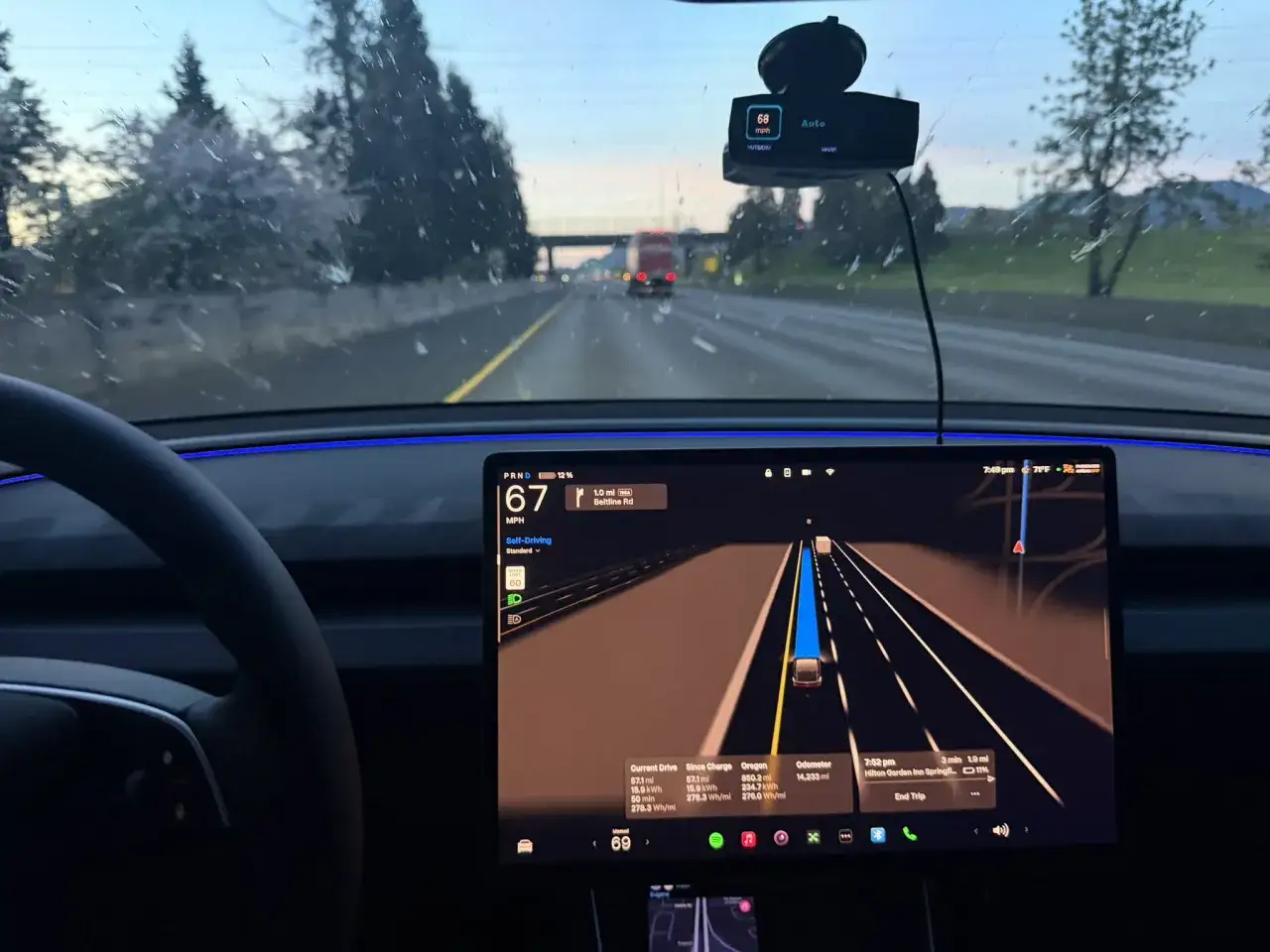 Interno di una Tesla con FSD attivo in Europa, visualizzazione della guida autonoma su autostrada al tramonto.