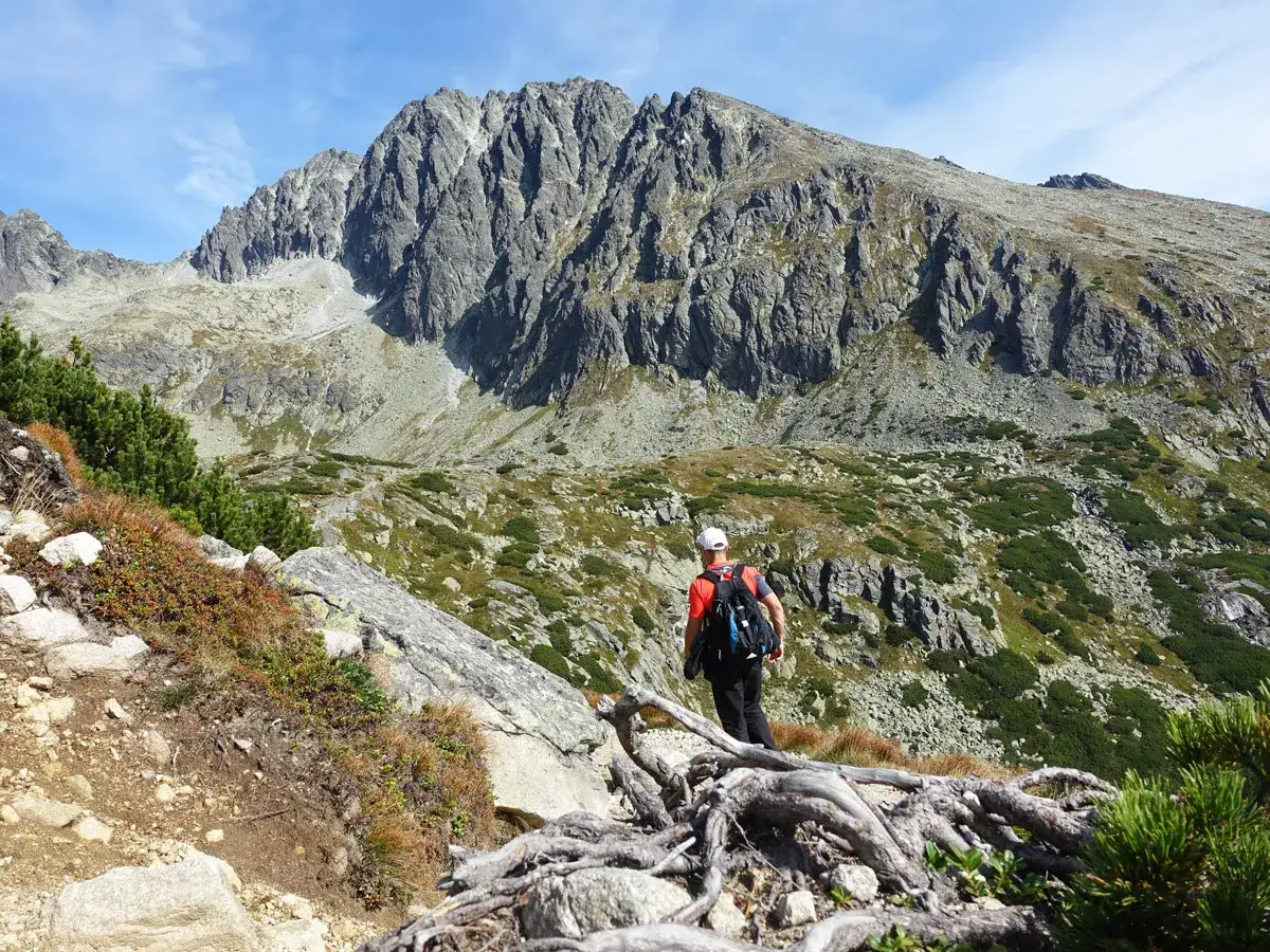 Wanderer im Tatra Gebirge auf einem steinigen Pfad, mit Blick auf zerkl&uuml;ftete Gipfel und gr&uuml;ne H&auml;nge.