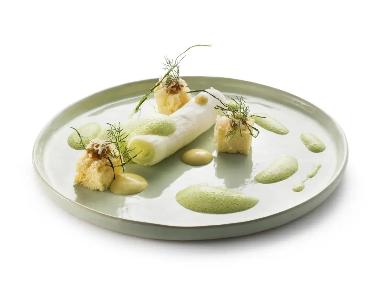 Poireaux &agrave; la cr&egrave;me, pr&eacute;sent&eacute;s avec des cubes de pain brioch&eacute;, des &eacute;clats de noix et une &eacute;mulsion verte sur une assiette pastel.