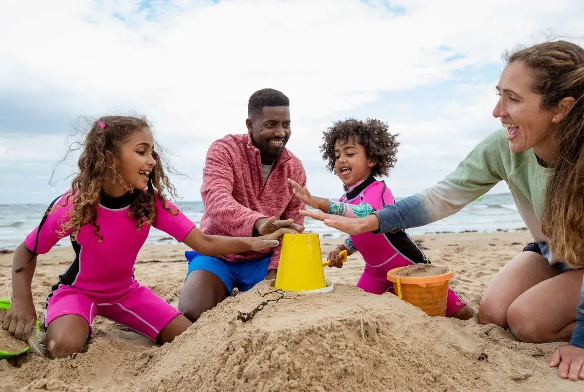 Une famille s'amuse à construire un château de sable, une scène joyeuse digne d'une animation colonie de vacances.