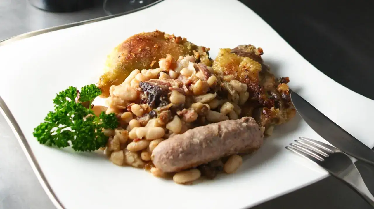 Un plato de el cassoulet con pollo crujiente, salchicha y judías blancas, adornado con perejil fresco.