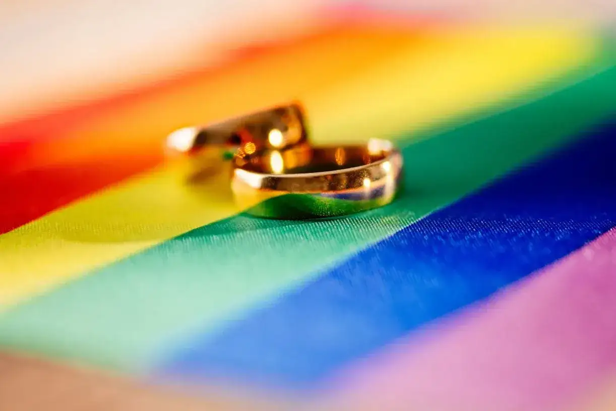 Dwa złote obrączki na tęczowym tle symbolizują piękny związek partnerski.