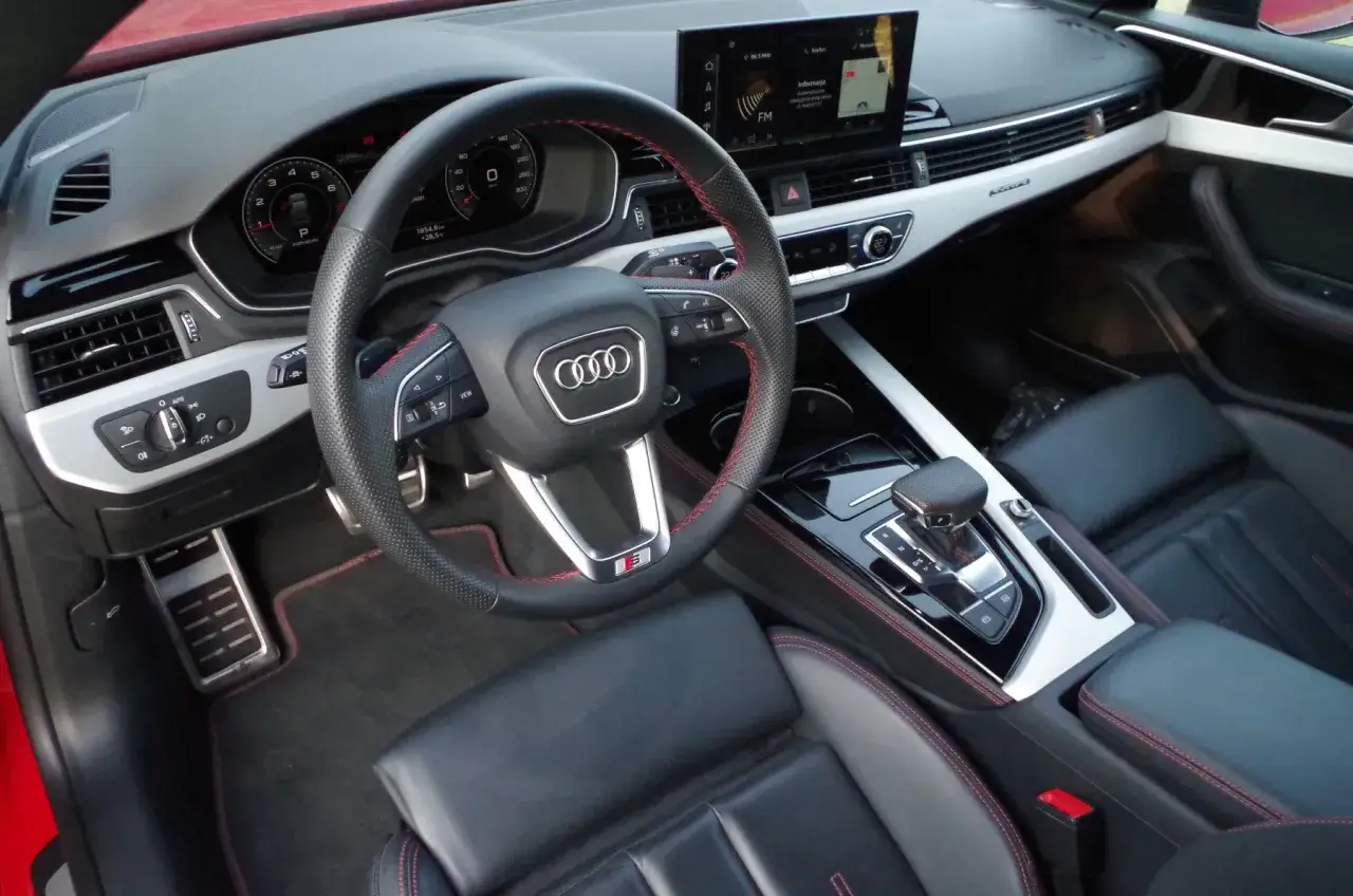 Wnętrze Audi A5 2.0 TFSI: czarna skóra z czerwonymi przeszyciami, sportowa kierownica, cyfrowe zegary i ekran multimedialny.