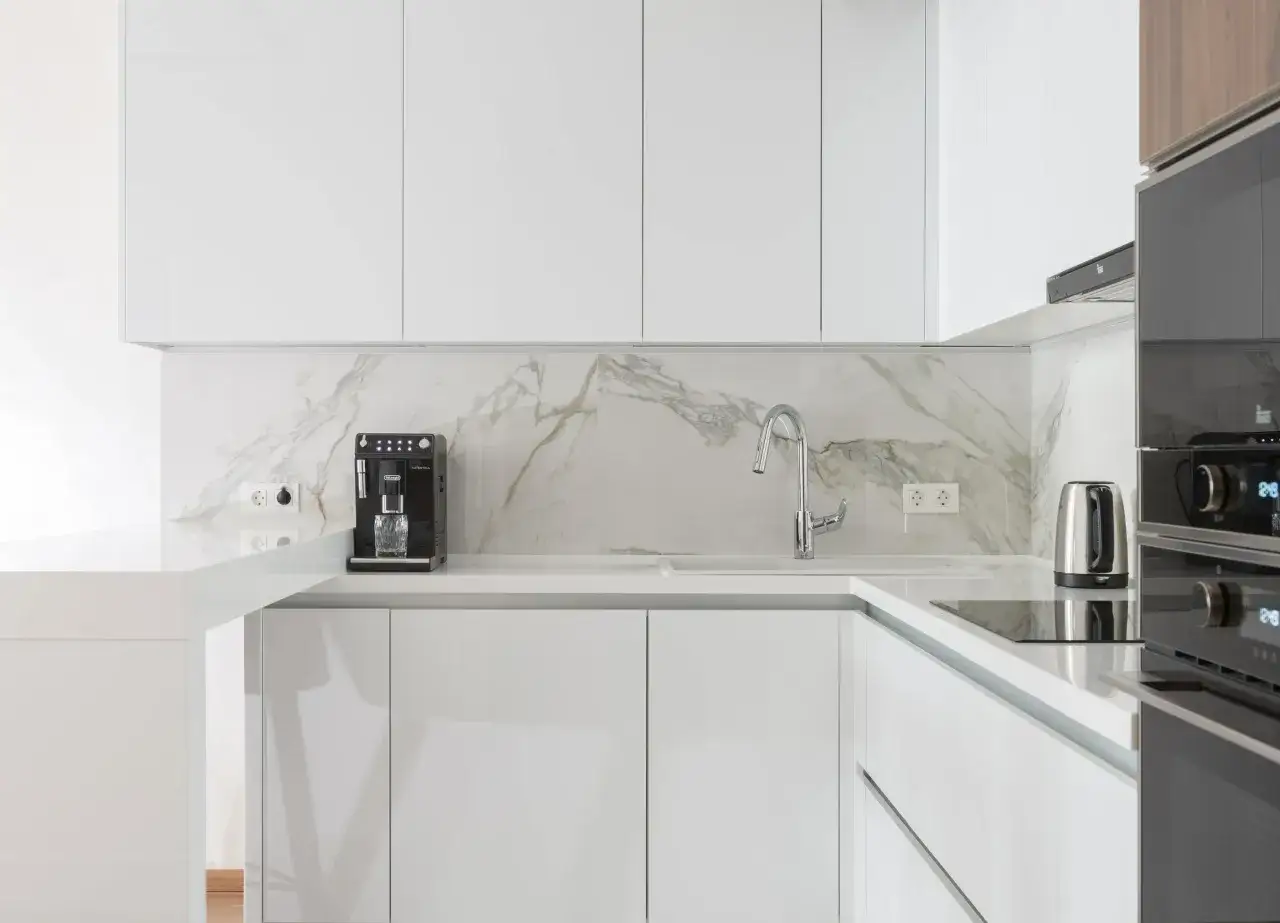 Cocinas blancas elegantes con encimeras de mármol, cafetera y hervidor.