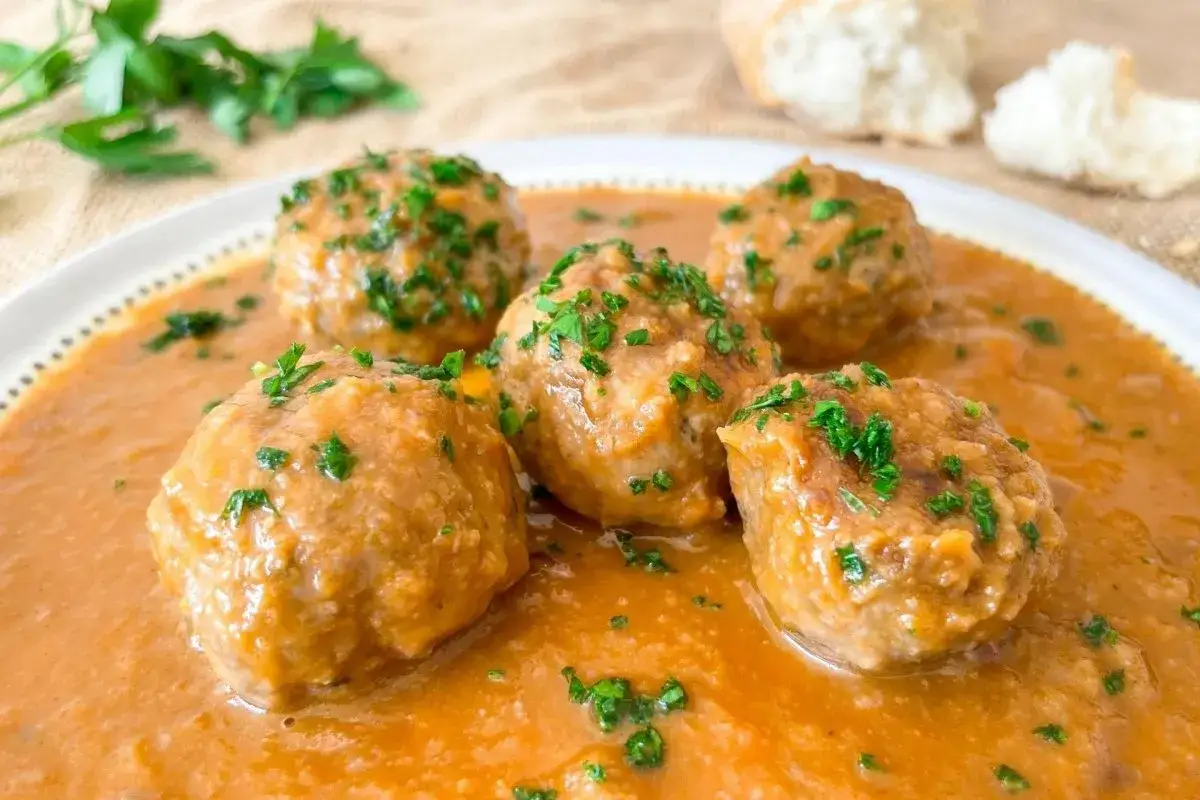 Cinco albóndigas al horno, jugosas y doradas, nadan en una rica salsa de tomate, espolvoreadas con perejil fresco. ¡Un plato casero irresistible!