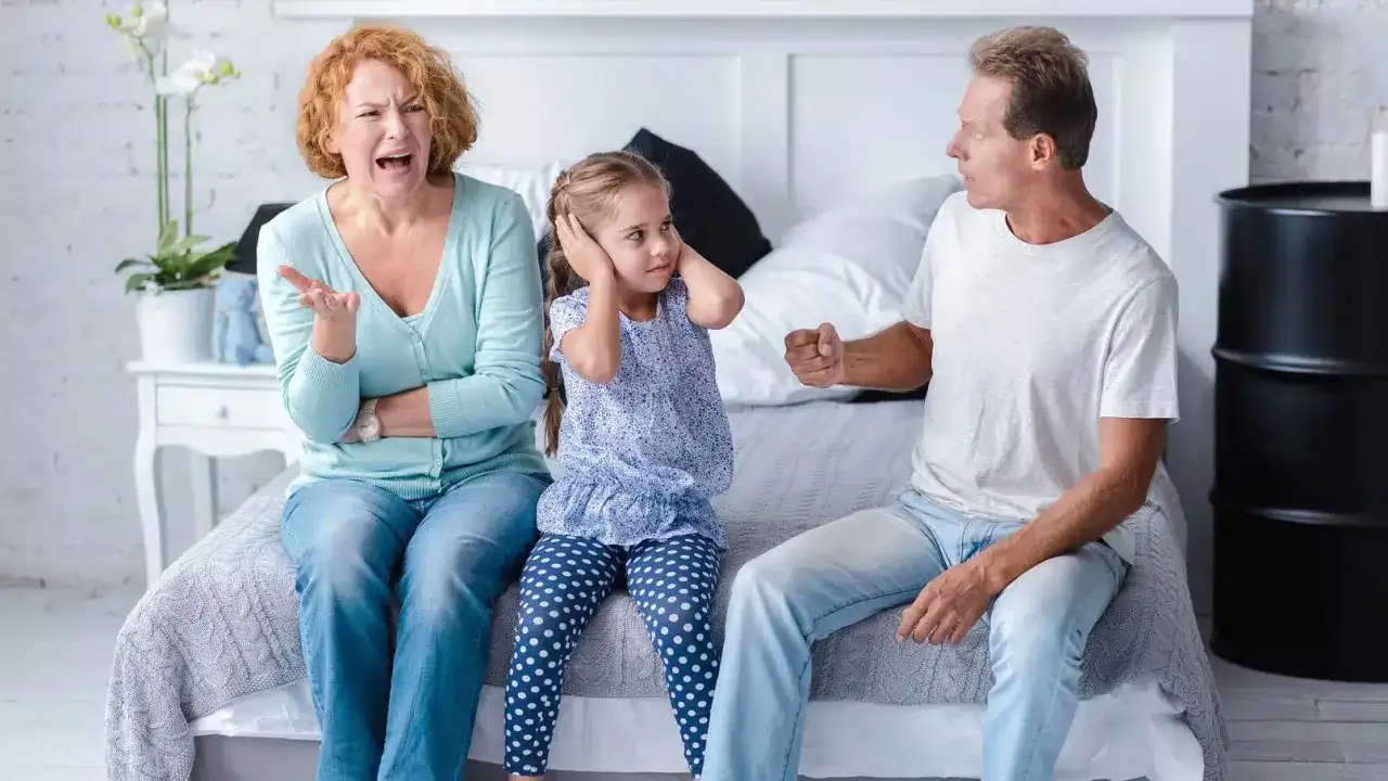 Una bambina si tappa le orecchie mentre i genitori litigano animatamente sul letto.