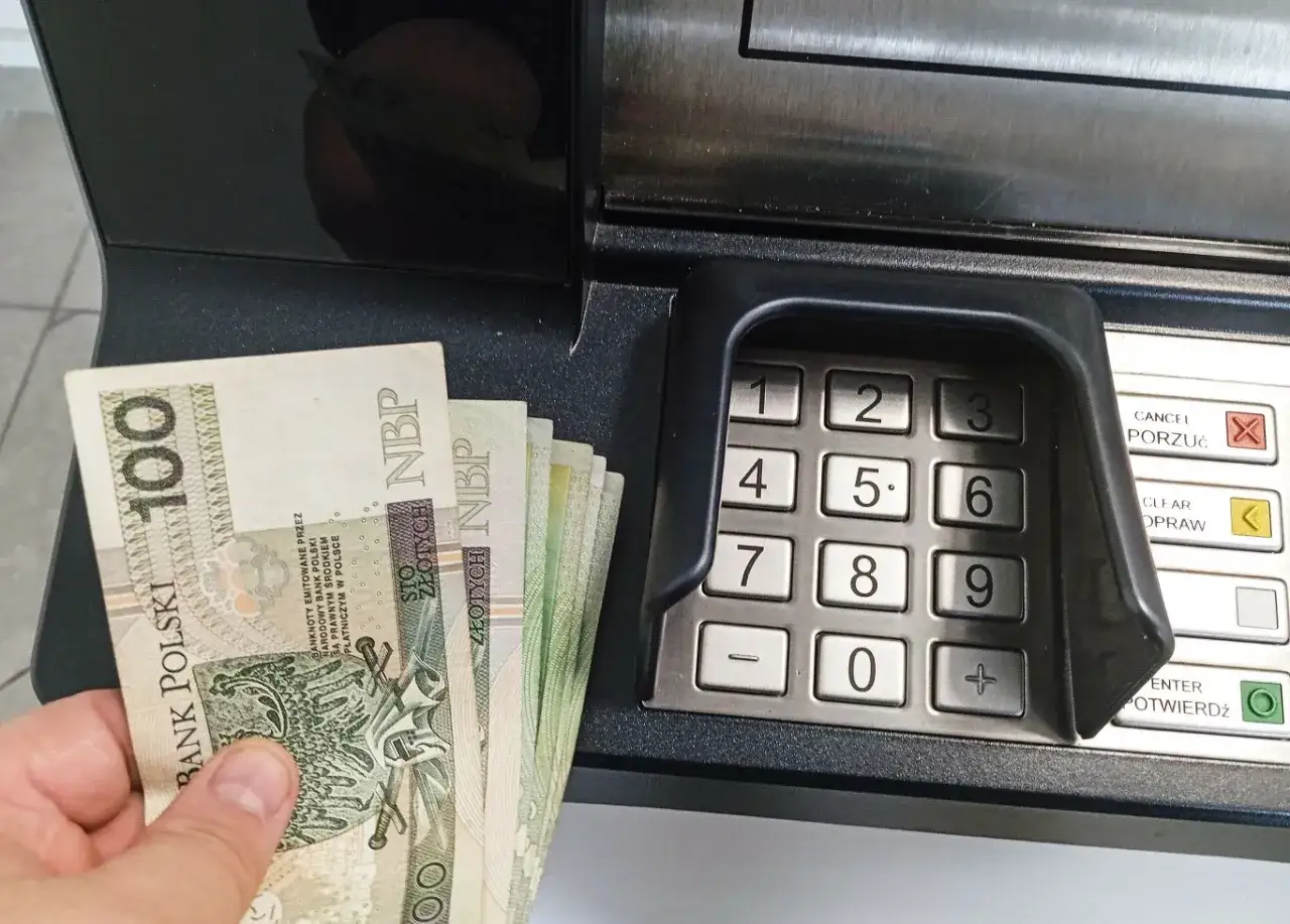 Dłoń trzyma banknoty 100 zł przy bankomacie. Zastanawiasz się, ile można wpłacić na konto?