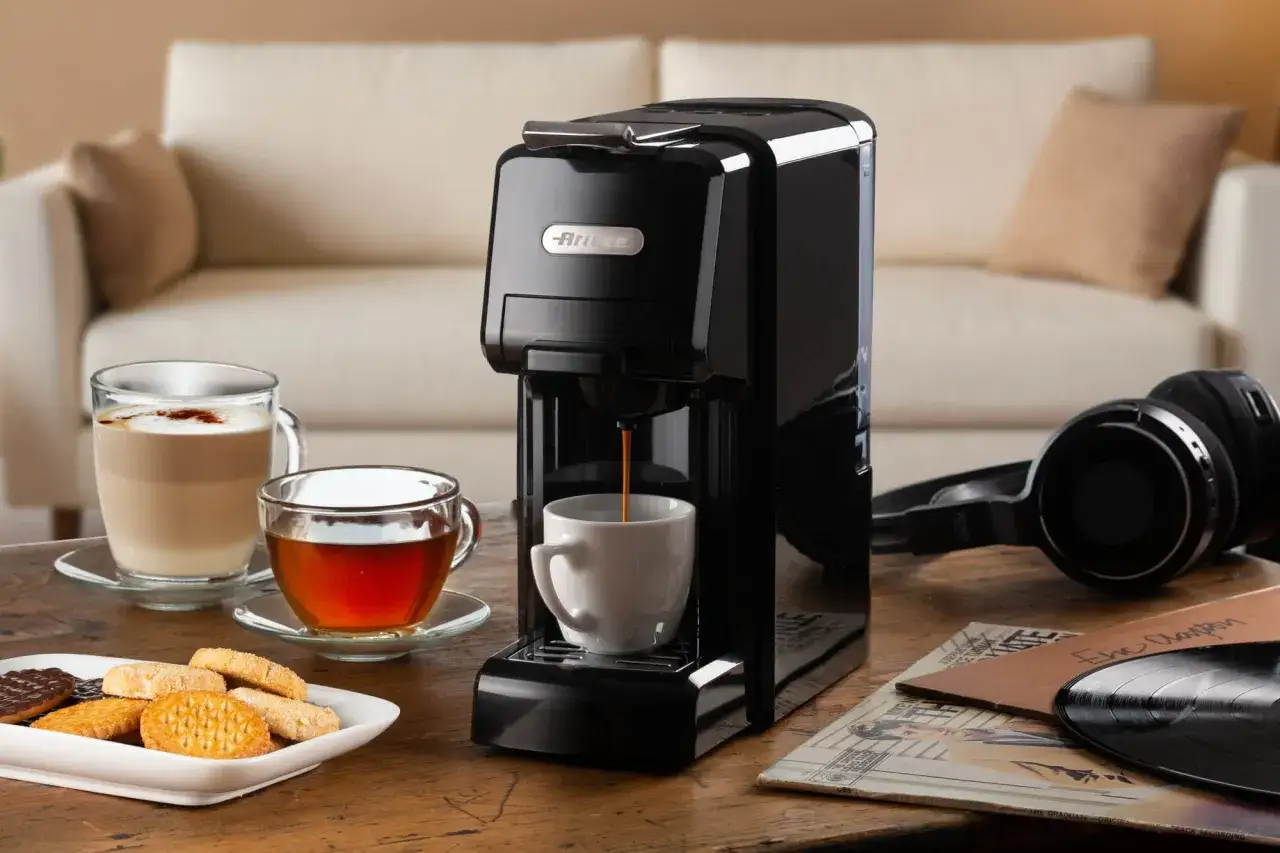 Macchina per caffè con cialde in azione, mentre un espresso riempie una tazzina. Accanto, un latte macchiato, tè, biscotti e vinili.