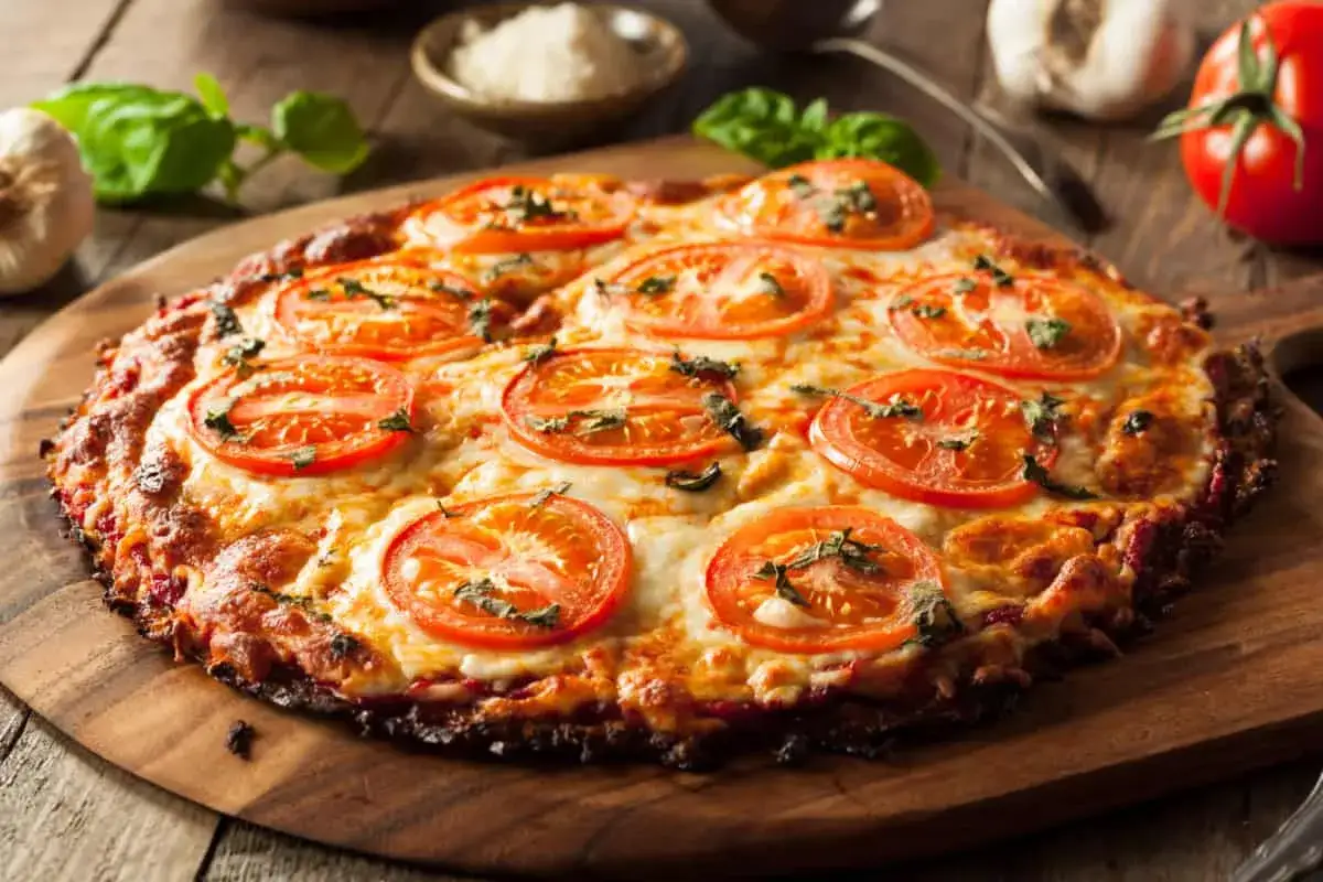 Deliciosa pizza de coliflor con queso derretido y rodajas de tomate fresco, adornada con albahaca.