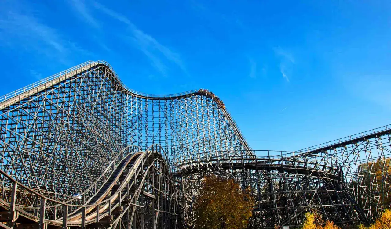 Drewniany rollercoaster w Heide Park, jedna z wielu ekscytujących atrakcji, pędzi po torach na tle błękitnego nieba.