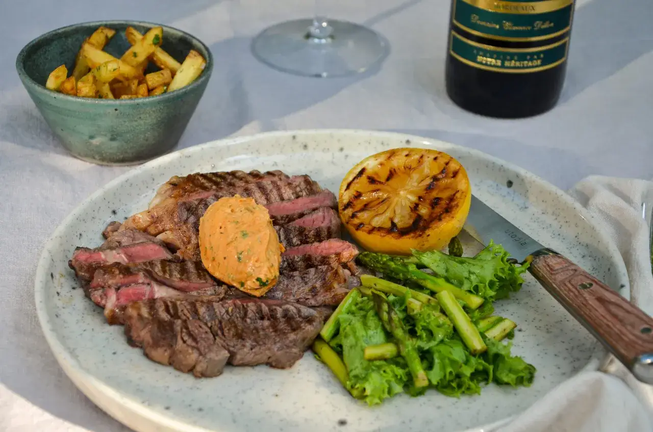 En saftig biff med en klick cafe de paris s&aring;s, serverad med pommes frites, grillad citron och gr&ouml;na gr&ouml;nsaker.