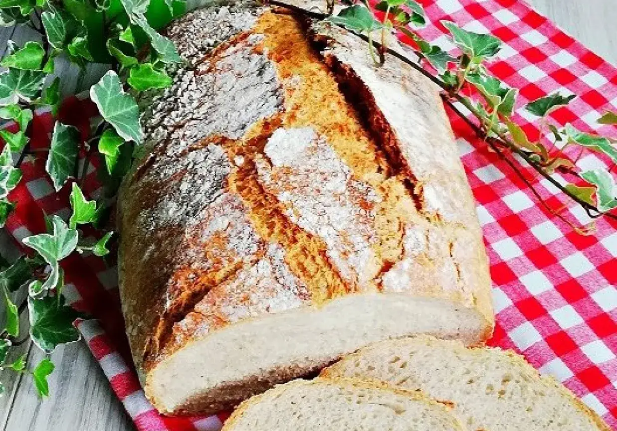 Chleb z amarantusem, świeżo upieczony, z chrupiącą skórką, pokrojony na kromki, leży na czerwono-białej kratce, ozdobiony zielonymi liśćmi.