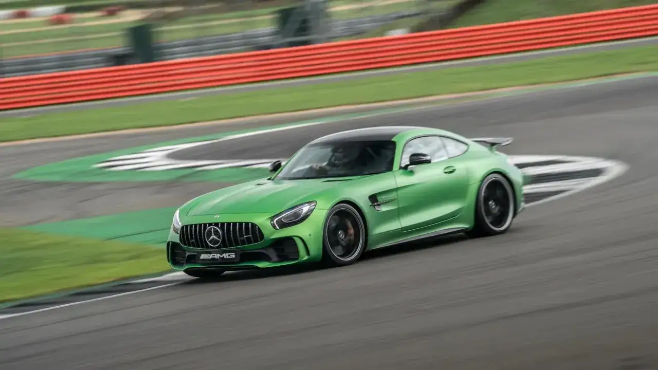 Un Mercedes GTR verde brillante acelera en una pista de carreras, con el conductor visible tras el volante.