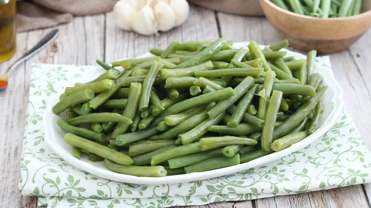 Fagiolini in padella, cotti al punto giusto, serviti su un piatto bianco con un tovagliolo decorato.
