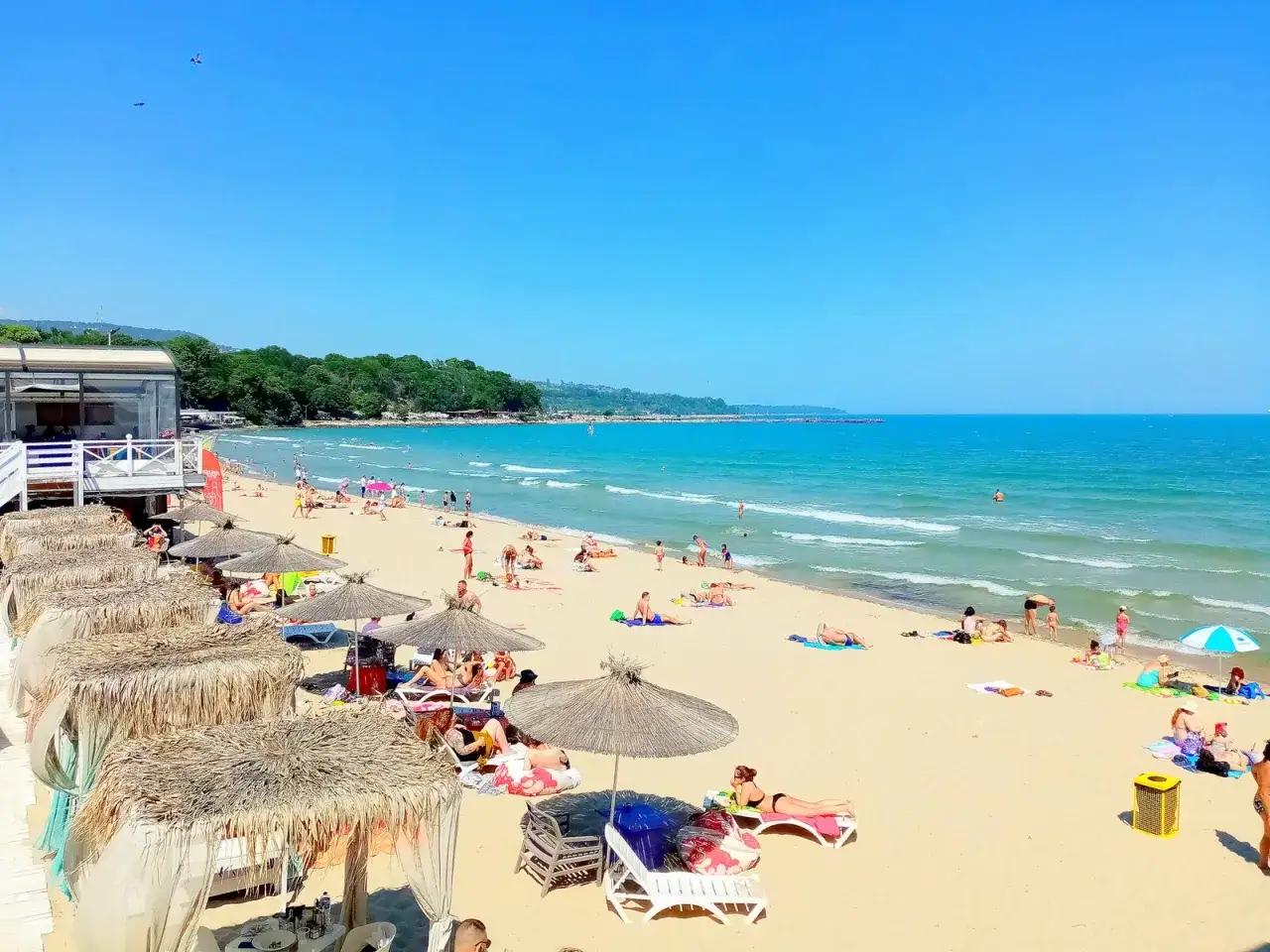 Słoneczna plaża z turystami i kawiarnią nad morzem. To dowód, że Bułgaria ma dostęp do morza.