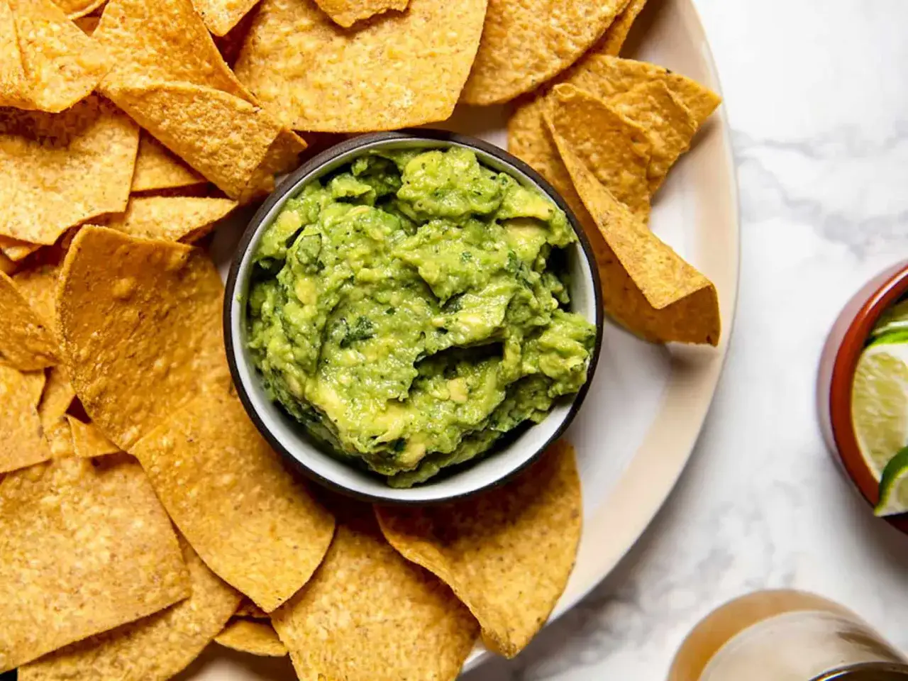 En skål med krämig guacamole omgiven av tortillachips. Perfekt för ett enkelt guacamole recept.