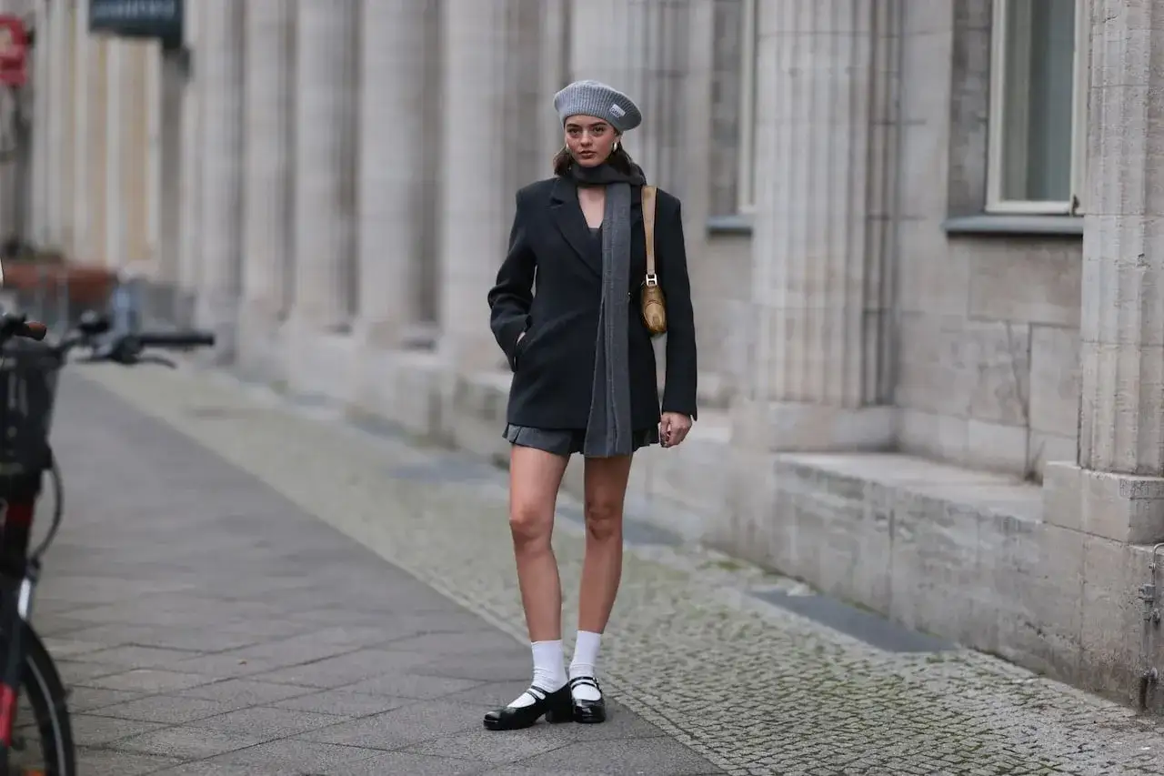 Mary Jean w szarej stylizacji z marynarką i spódniczką, na ulicy z kolumnami.