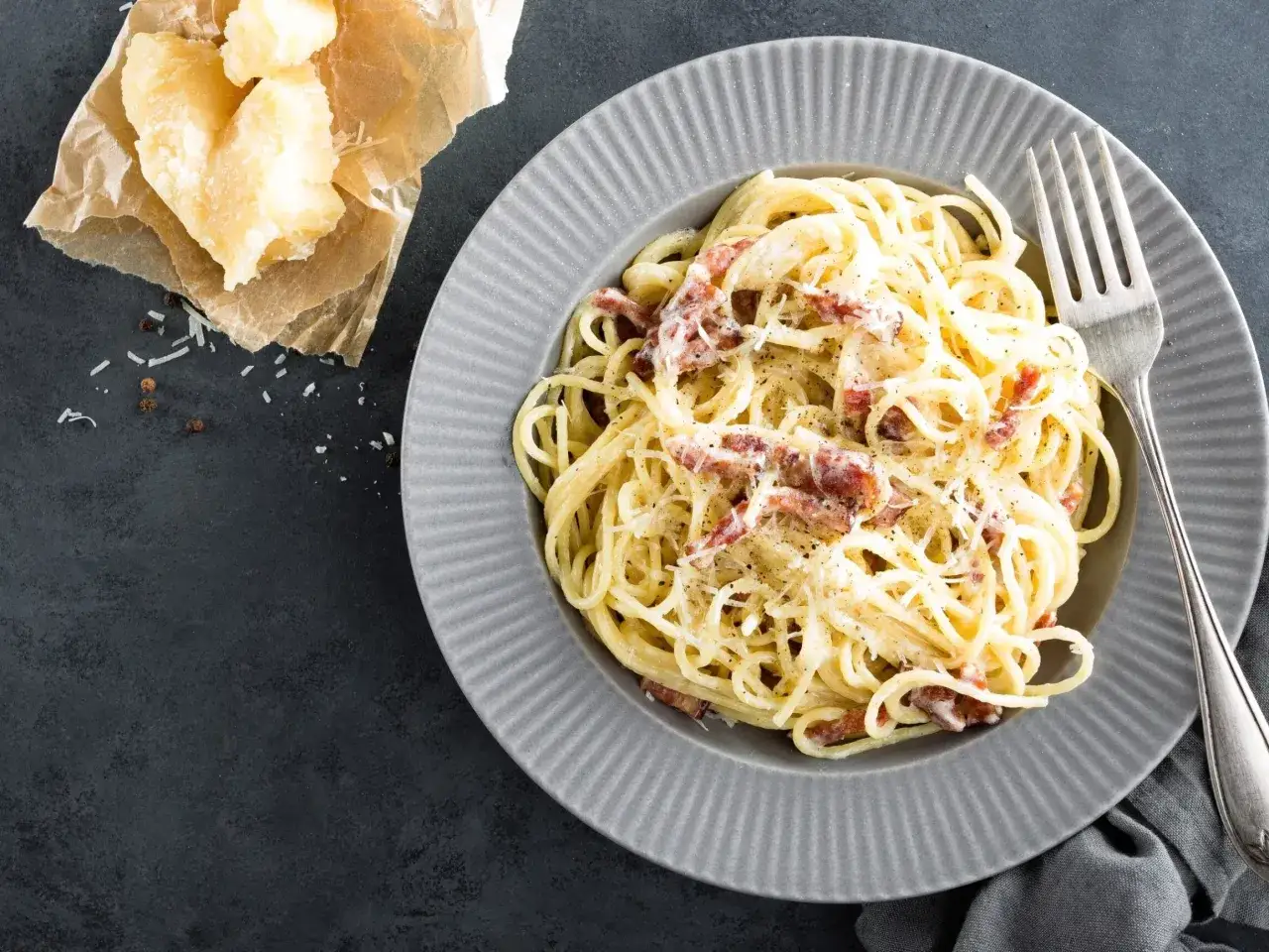 Pyszna carbonara z parmezanem, idealny ser do carbonary. Obok talerza kawałek sera i pieprz.