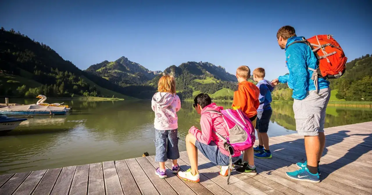 Famille profitant d'une journée ensoleillée au bord d'un lac, paysage montagneux. Parfaites vacances scolaires Fribourg.
