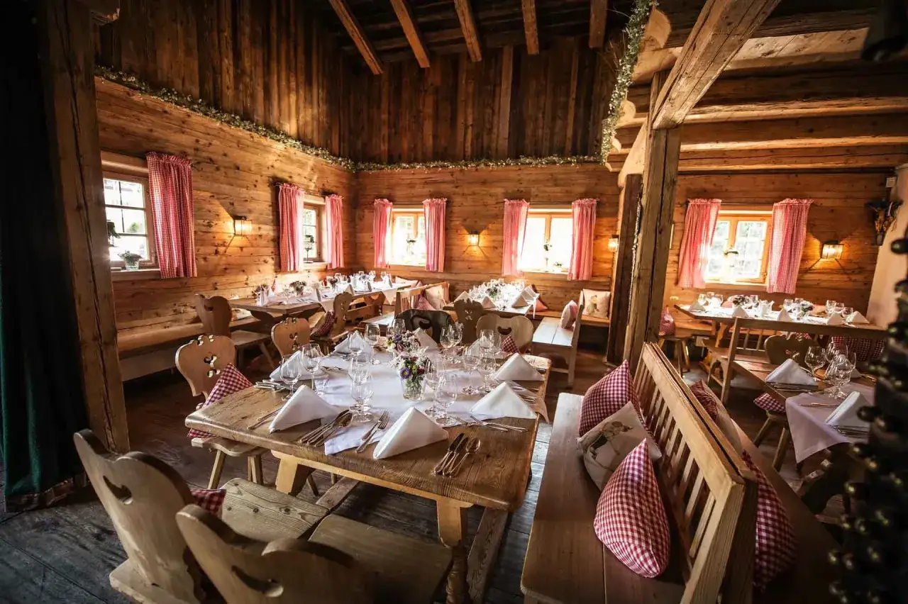 Gemütliche Holzhütte, festlich gedeckte Tische für eine Egerner Alm Hochzeit. Rote Karovorhänge und Blumen schmücken den rustikalen Raum.