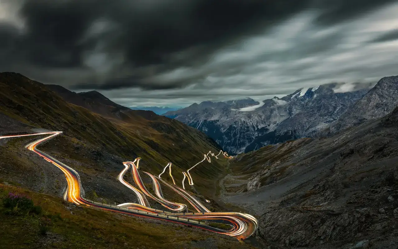 Nocne światła samochodów tworzą świetlne wstęgi na serpentynach Passo dello Stelvio. Kiedy otwarta, droga ta zachwyca widokami.