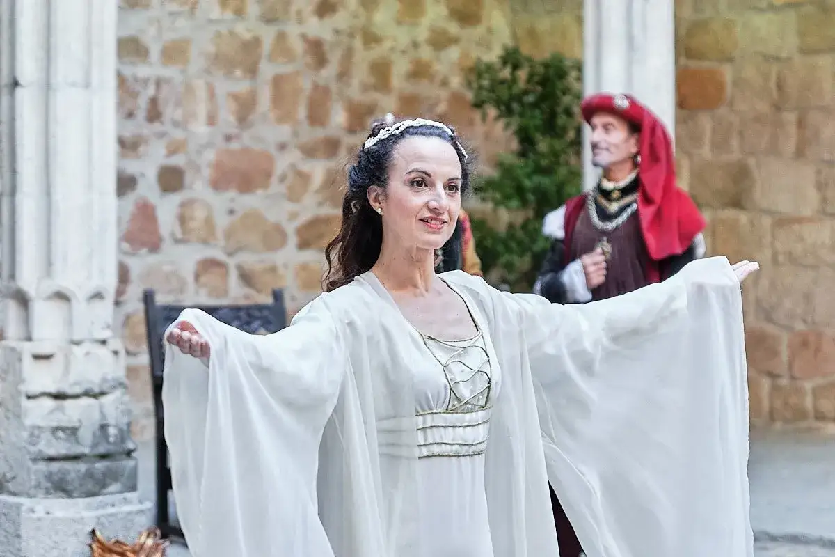 Una mujer con un vestido blanco y una diadema, como si fuera un personaje de Francisco de Aldana, sonr&iacute;e. Detr&aacute;s, un hombre con atuendo hist&oacute;rico.
