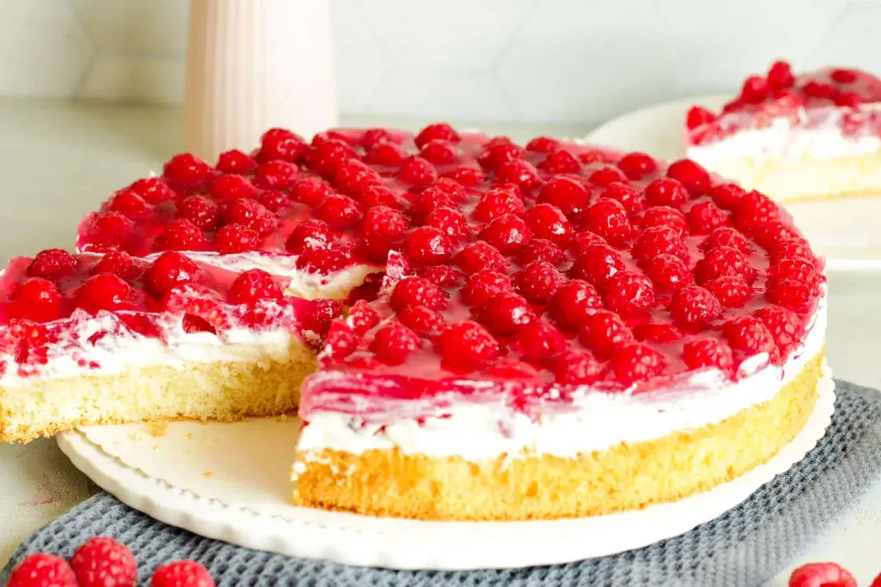Ein saftiger Himbeerkuchen mit gefrorenen Himbeeren, bedeckt mit glänzendem Tortenguss und einer cremigen Füllung.