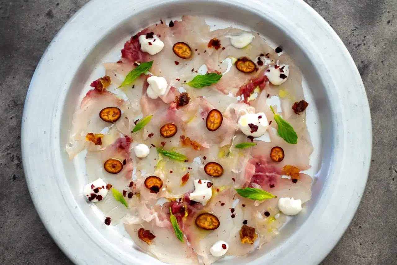 Delicati antipasti di pesce crudo, guarniti con cubetti di kumquat, gocce di crema bianca e foglioline di menta.