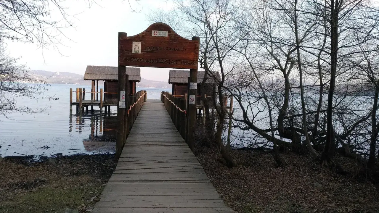 Pontile in legno sul lago di Viverone, con piccole capanne sull'acqua e alberi spogli.