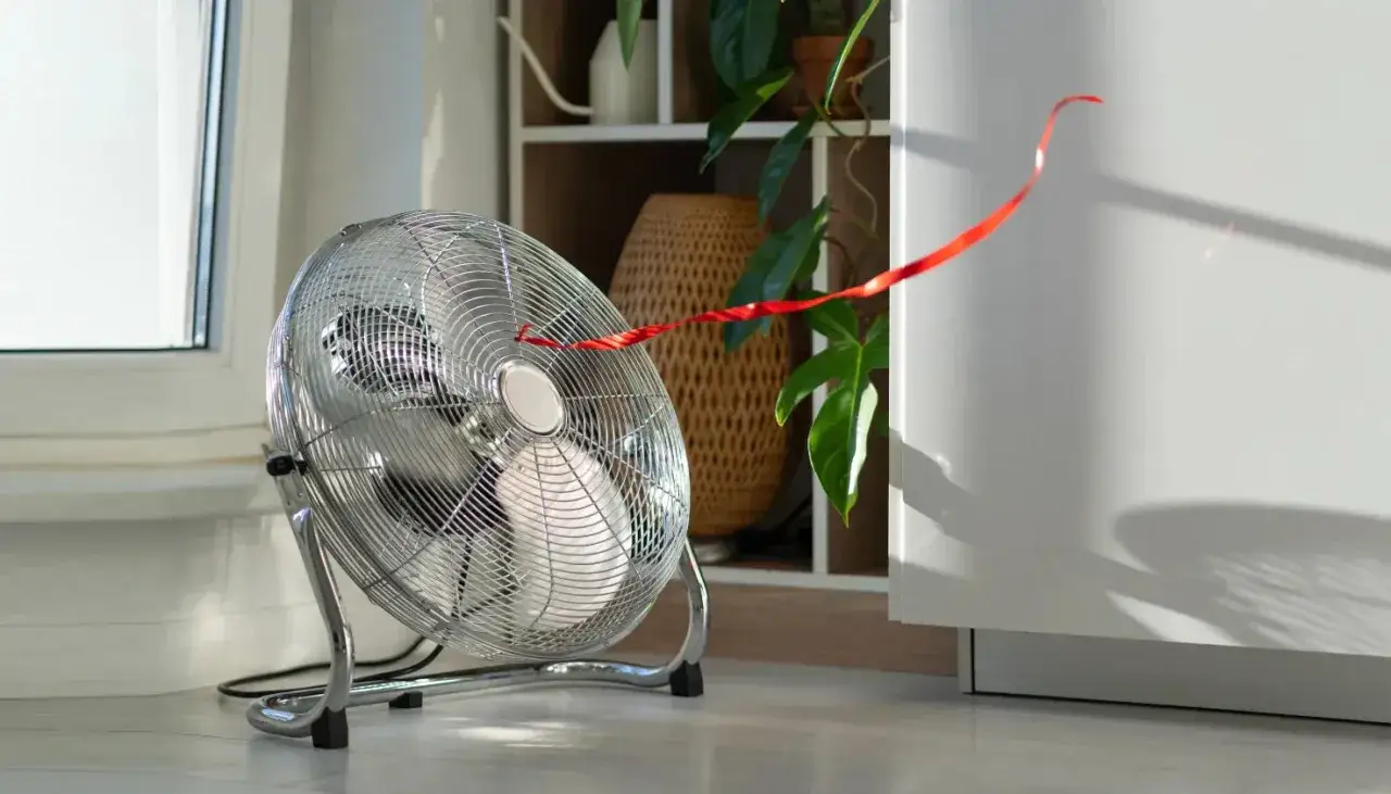 Un ventilador metálico con una cinta roja ondeando muestra cómo refrescar una habitación.