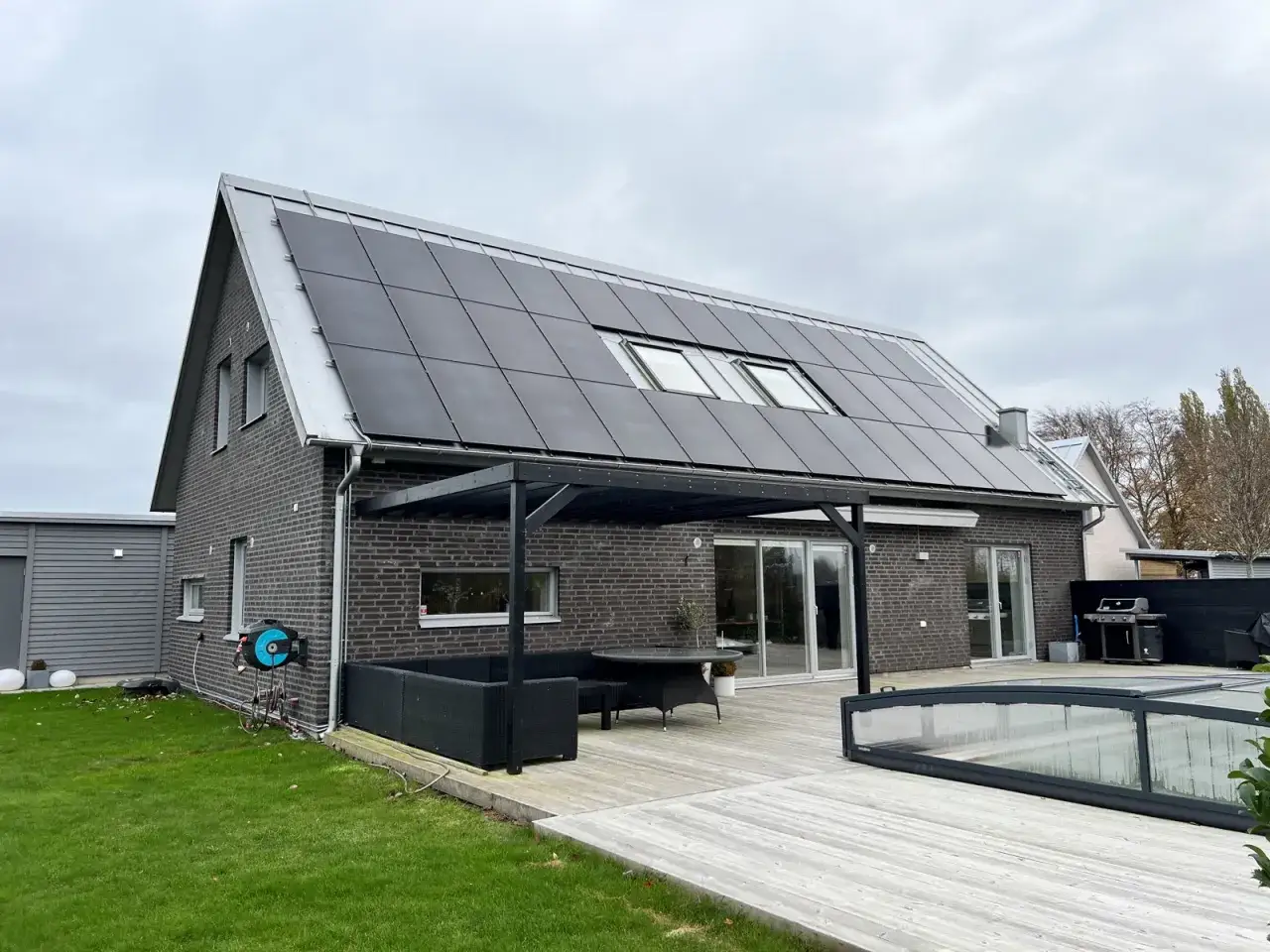 Hus med solceller p&aring; taket, installerade av Solceller Syd AB. Tr&auml;d&auml;ck med utem&ouml;bler och pool.