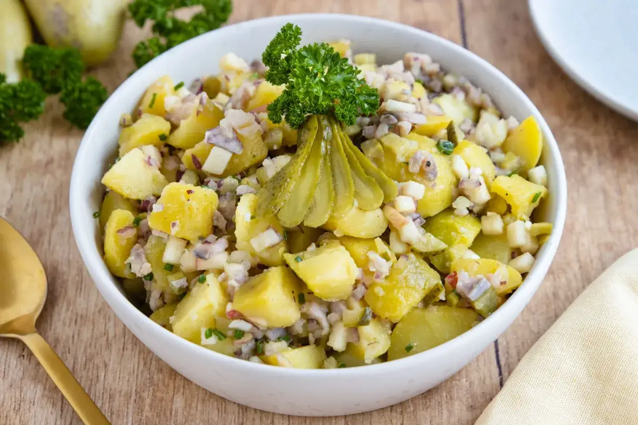 Schlesischer Kartoffelsalat mit Gurken, Zwiebeln und Petersilie, garniert mit Gewürzgurken. Ein Klassiker, der auf jedem Tisch gut aussieht.