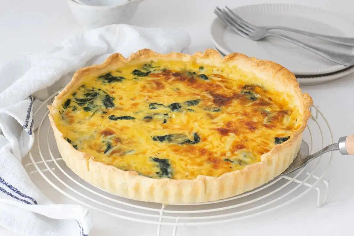 Un delicioso quiche de espinacas reci&eacute;n horneado, con masa dorada y relleno cremoso, listo para ser servido.