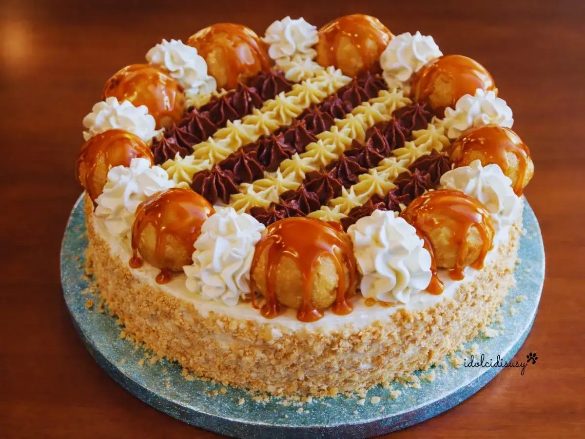 Una magnifica torta Saint Honoré, decorata con bignè caramellati, panna montata e riccioli di cioccolato e crema.