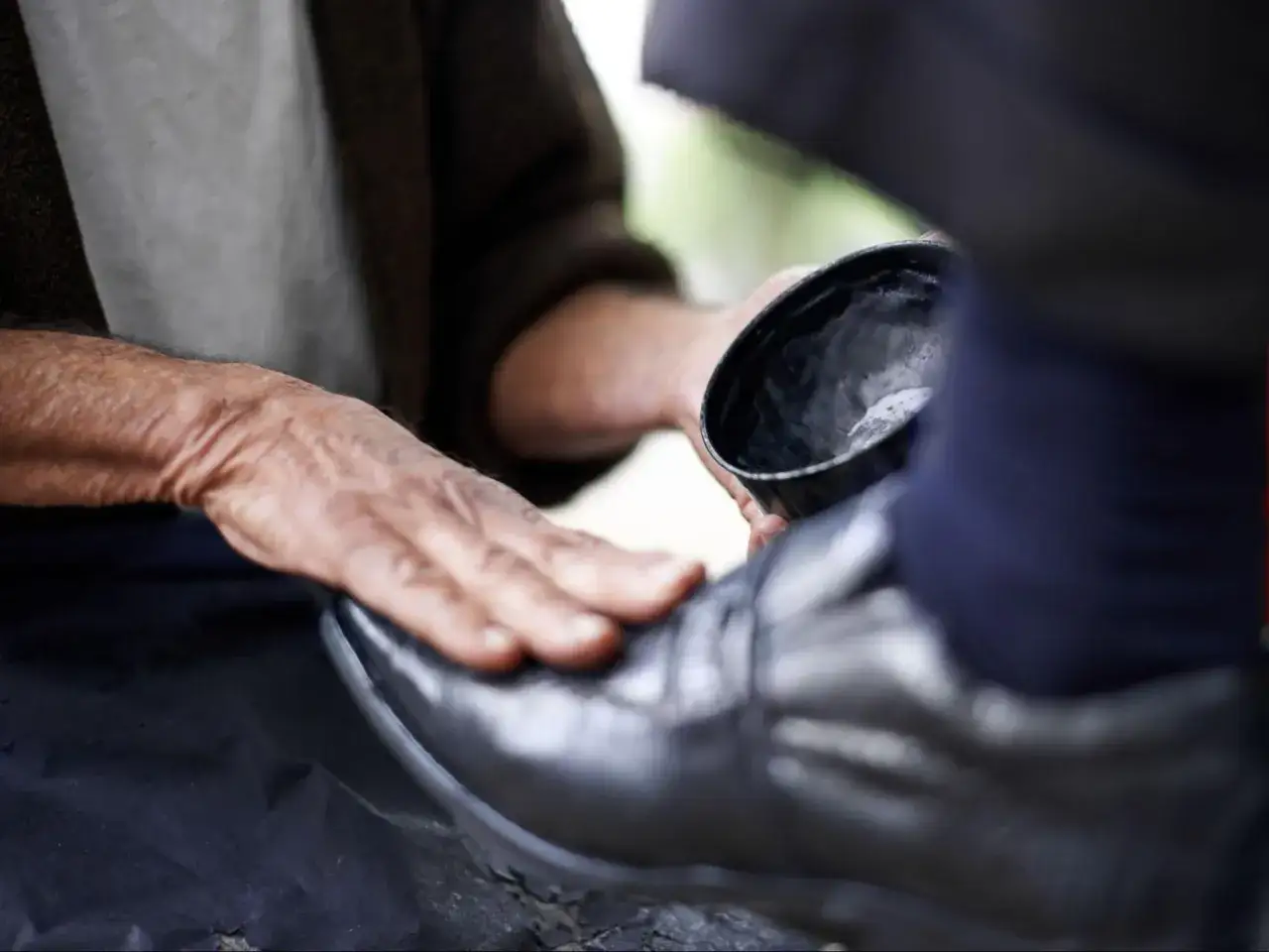 Manos cuidadosas aplicando betún para limpiar zapatos piel.