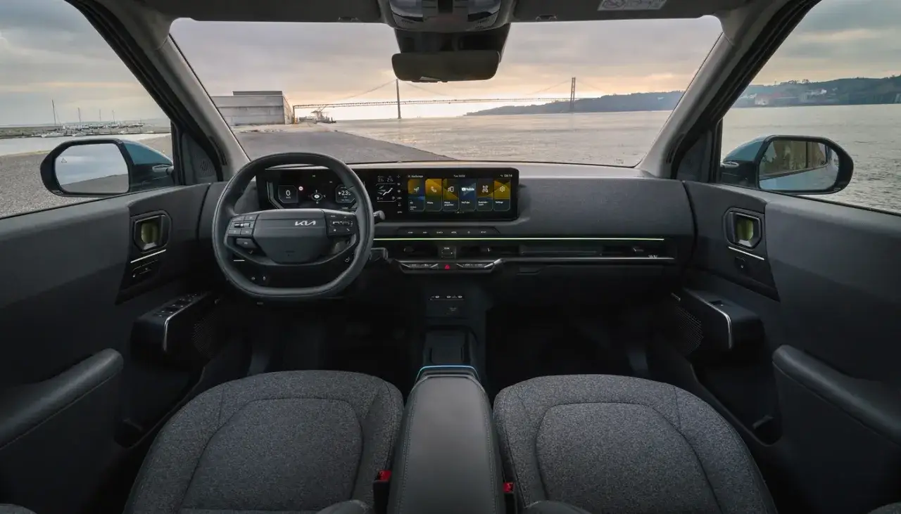Interior del ev2 kia con pantalla t&aacute;ctil, volante moderno y vista a un puente sobre el agua.