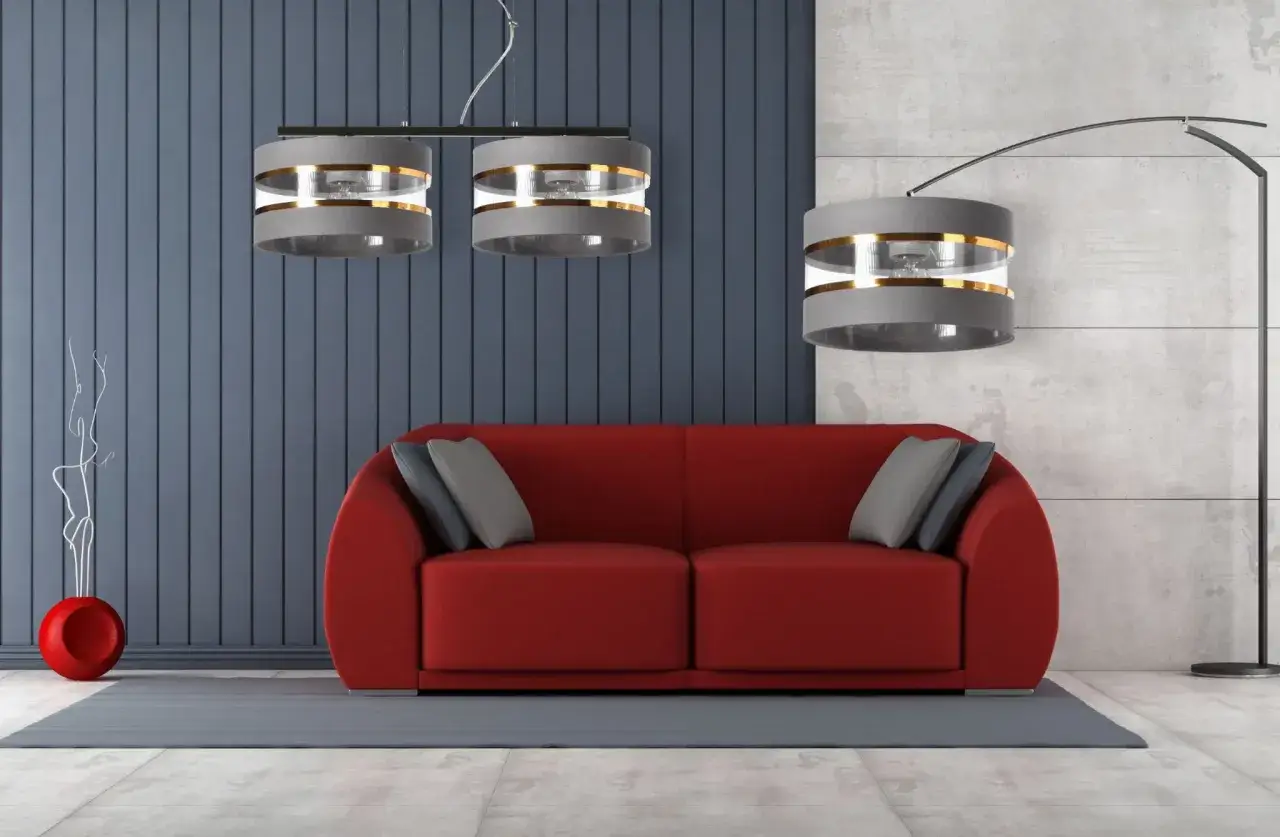 Nowoczesne klosze do lamp stojących i wiszących w szarym kolorze ze złotymi akcentami, tworzące elegancką oprawę dla czerwonej sofy.