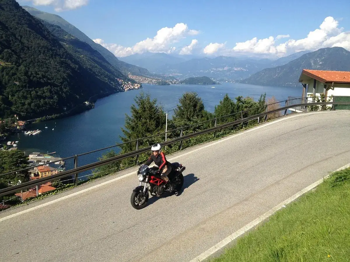 Una persona in moto percorre una strada panoramica con vista sul lago di Como.